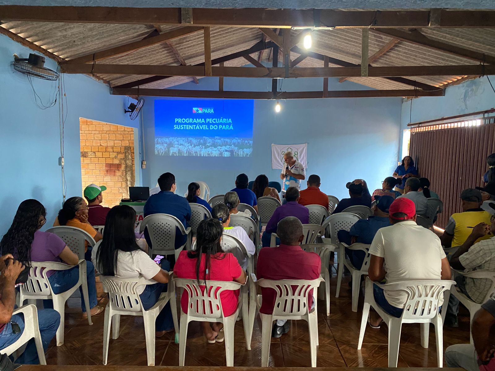 Imagem mostra público em cadeiras brancas de costas, assistindo programação de oficina 
