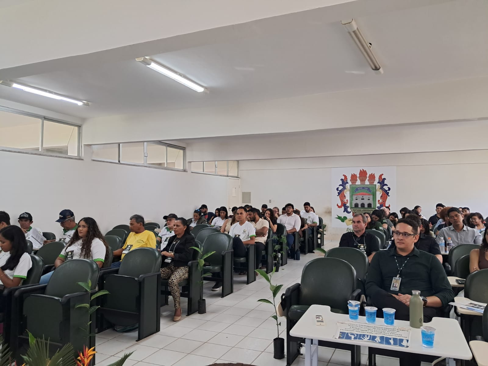 Imagem mostra auditório com dezenas de pessoas sentadas nas cadeiras, homens e mulheres, a maioria jovens
