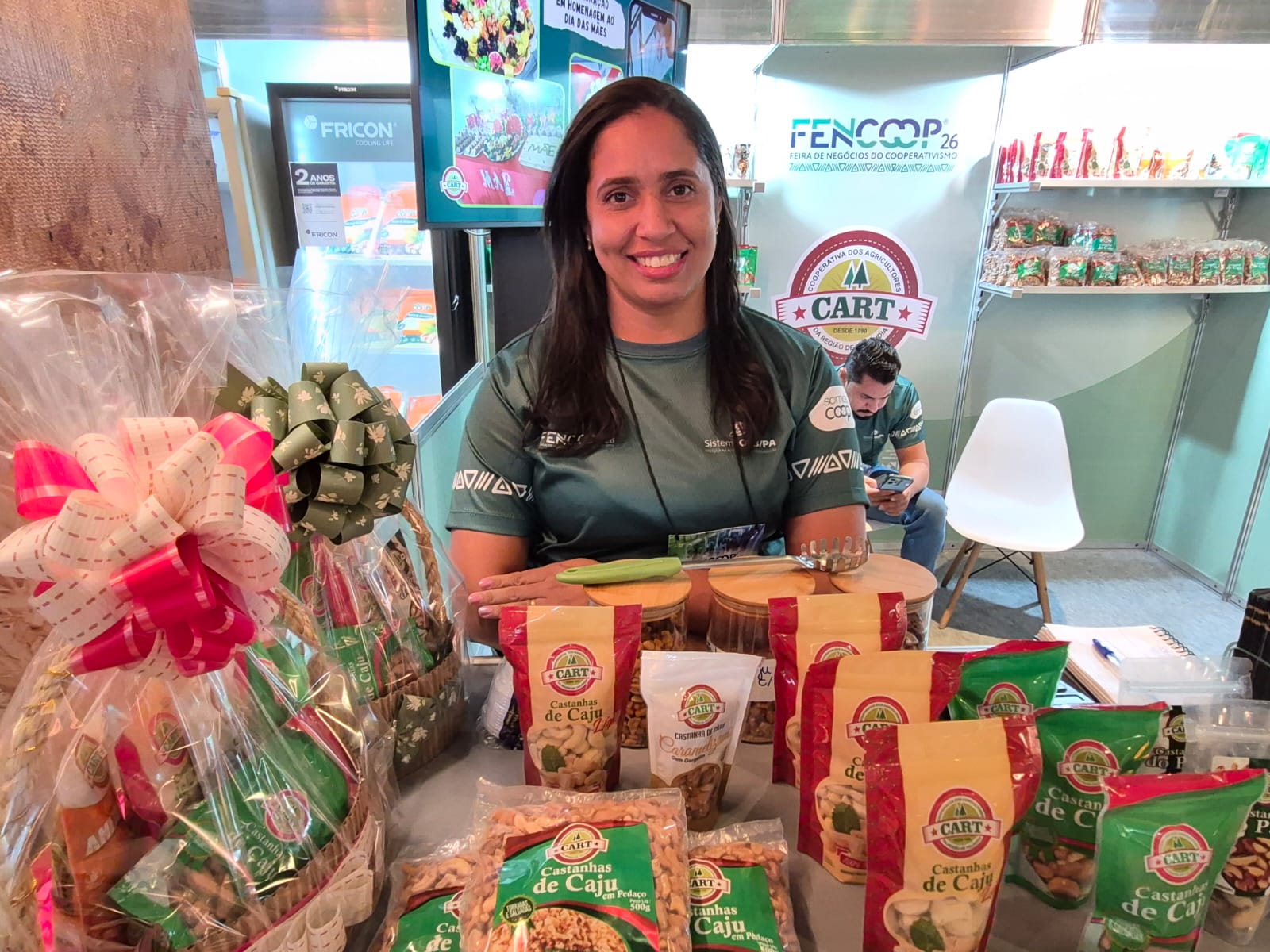 imagem mostra mulher de meia idade, cabelos lisos, camisa verde, em estande de exposição de produtos 