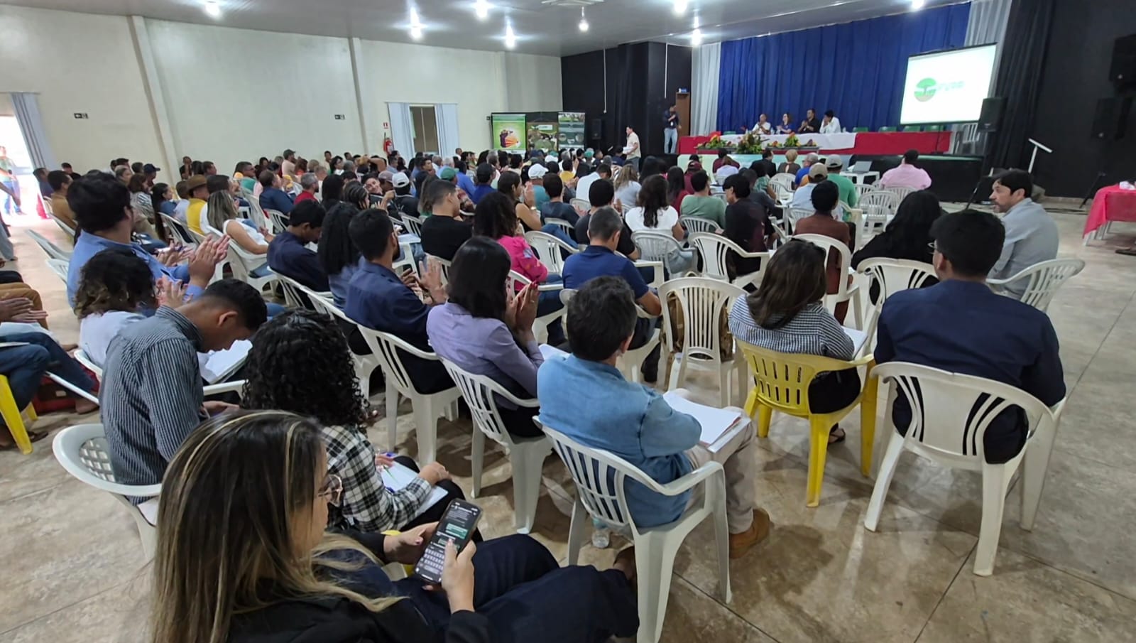Imagem mostra auditório lotado com pessoas sentadas de frente para um palco com telão