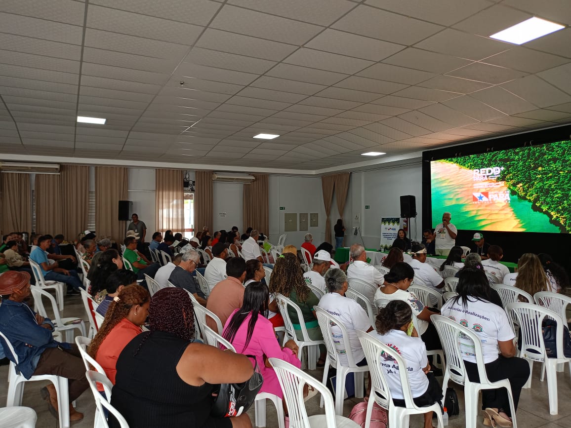 imagem mostra auditório com várias pessoas sentadas assistindo informações em um telão