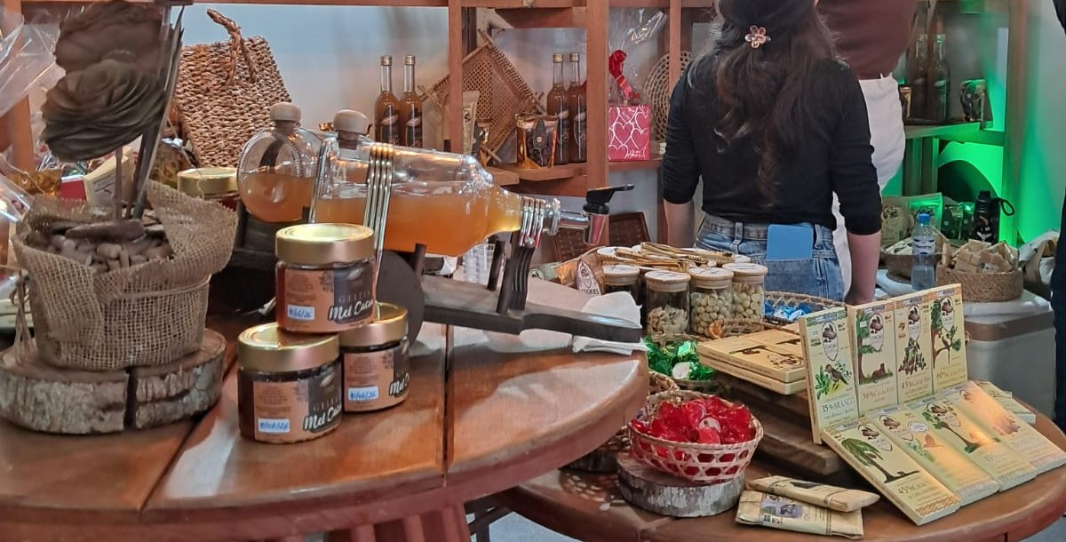 Imagem mostra mesa de estande cheia de produtos como geleias, doces, licor e outros produtos derivados do cacau 
