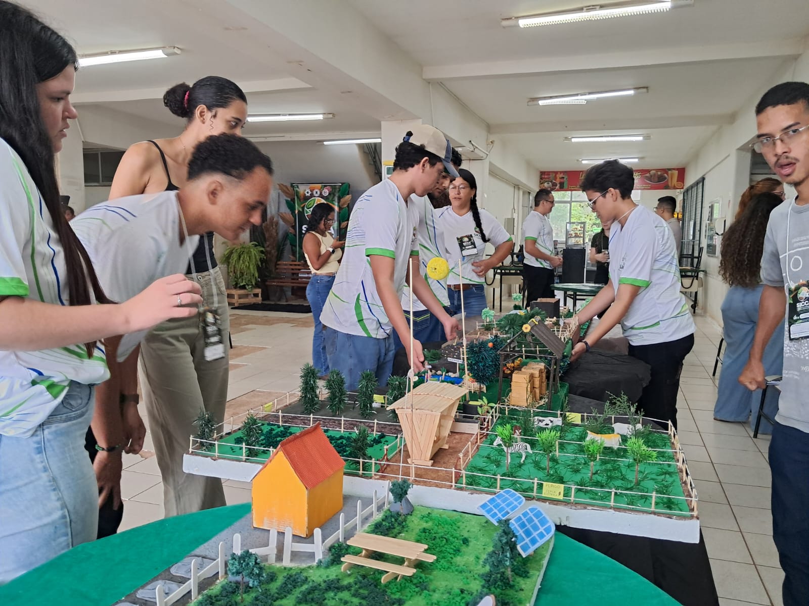 Imagem mostra estudantes observando maquetes sobre mesas em exposição