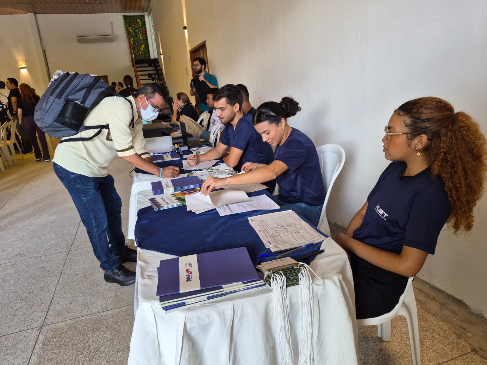 Imagem mostra homem assinando documento em mesa de credenciamento 