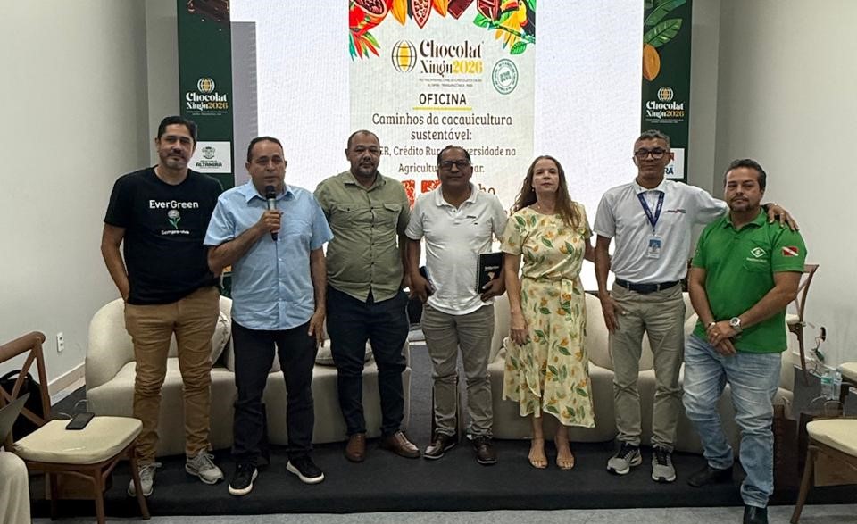 imagem mostra grupo de 7 pessoas, entre enles uma mulher, lado a lado, com um deles falando ao microfone